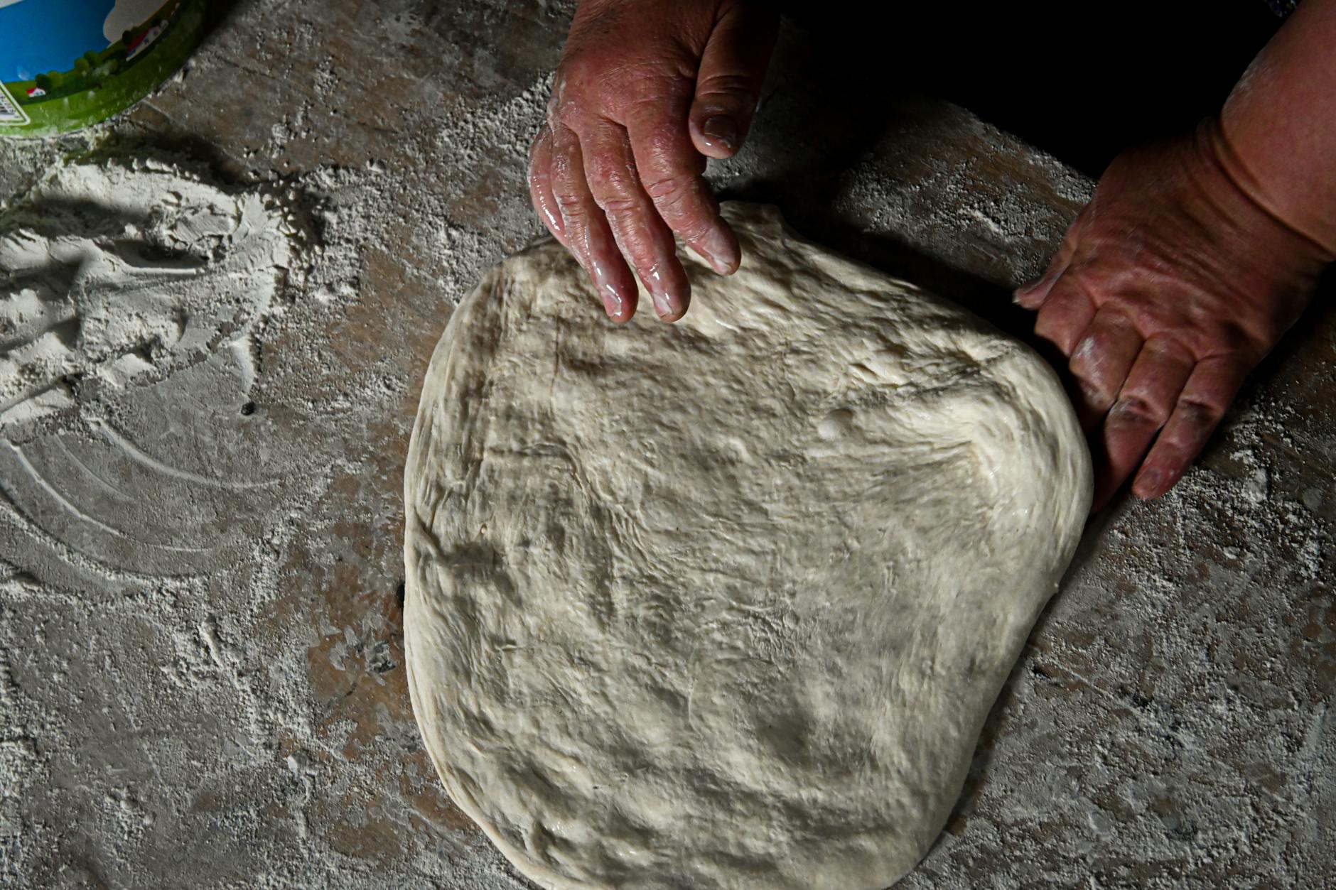 Pizzateig über Nacht – Hände ziehen den gereiften Pizzateig aus