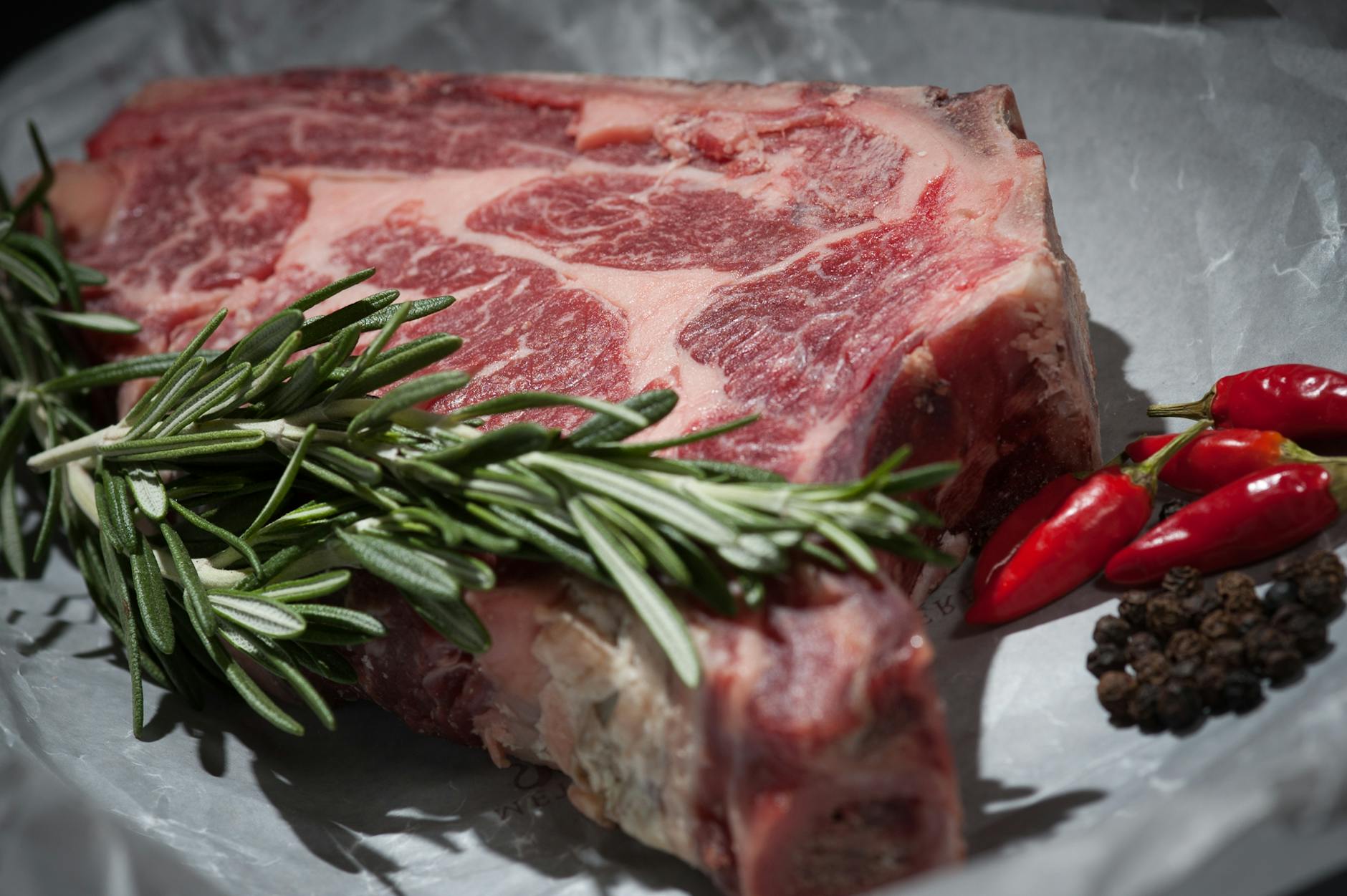 Steak braten – rohes Rib-Eye mit Rosmarin und Pfeffer auf dem Brett